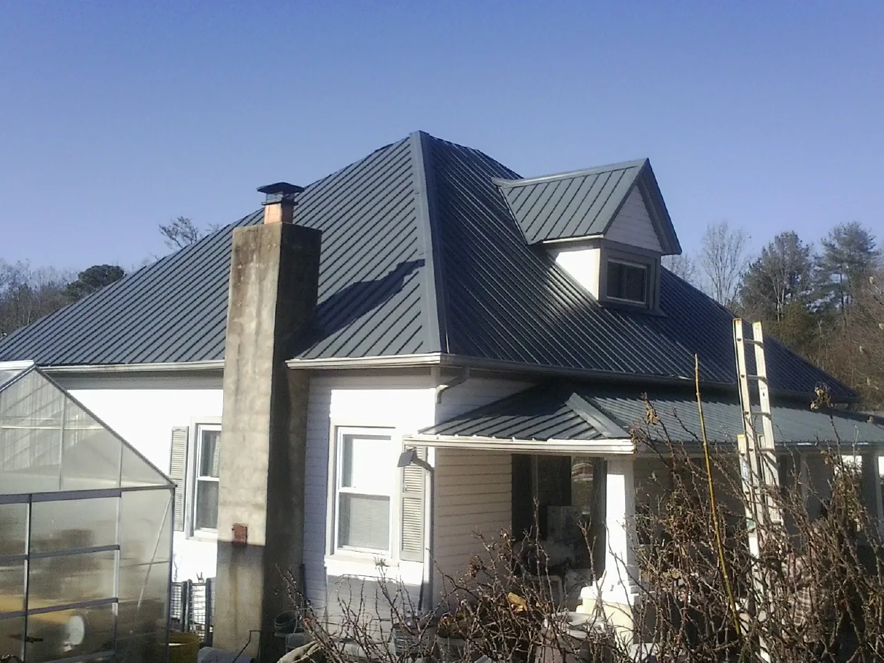 Dark blue standing seam metal roof on a white farmhouse with dormer — Slate & Tile Roof Repair by Roofing Brothers in Oneonta