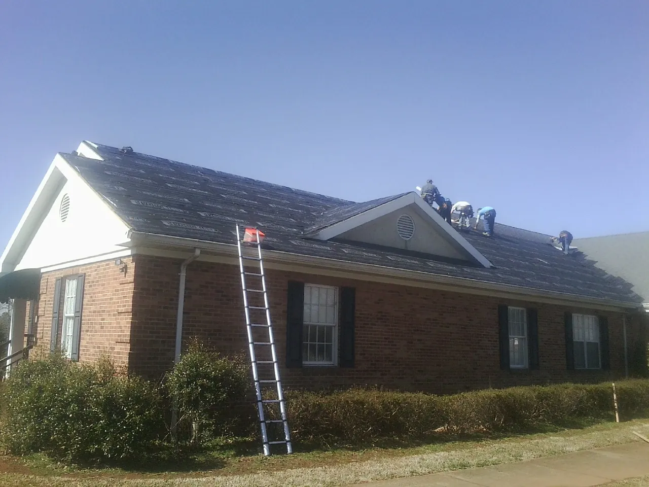 Crew tearing shingles off a brick ranch roof with a ladder set — Metal Roof Repair work by our crew in Oneonta