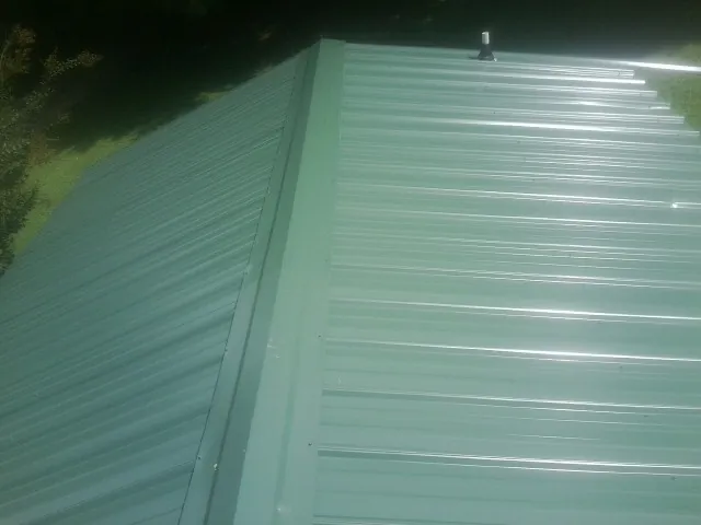 New green metal panels meeting at the ridge of a roof — Flat Roof Repair work by our crew in Oneonta