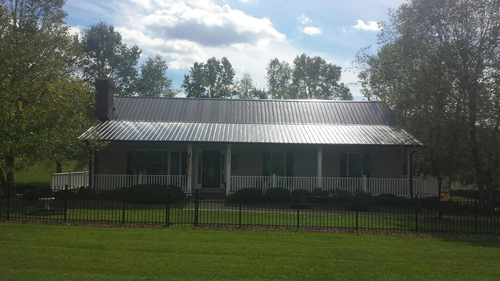 Gray metal roof on a brick ranch with a full width front porch — Gutter Guard Installation work by our crew in Oneonta